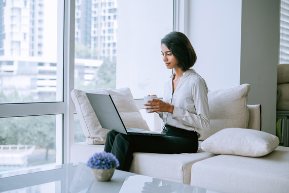 Woman sitting on couch using laptop and holding a mug