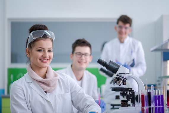 Three smiling scientists in a laboratory with a microscope