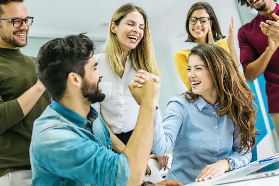 Group of coworkers celebrating success with a strong handshake in office