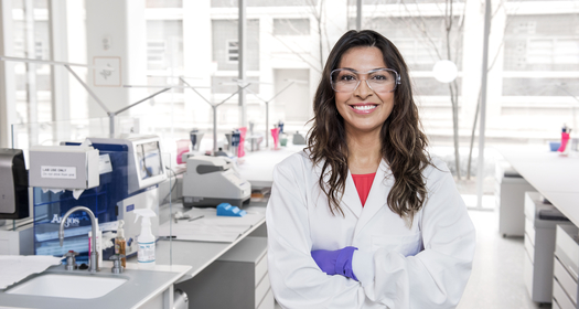 Smiling scientist in lab coat and safety glasses in laboratory
