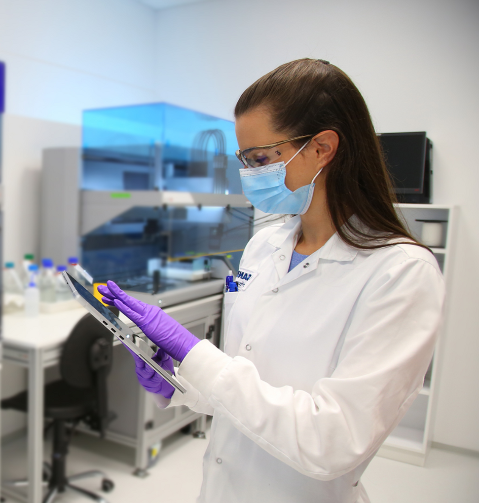 Znanstvenica z masko in rokavicami uporablja tablico v laboratoriju