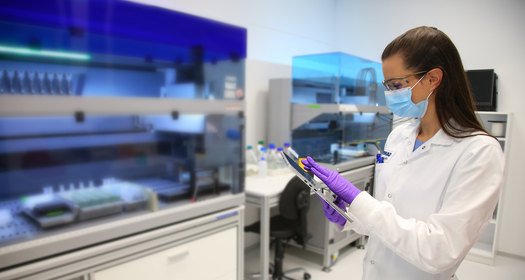 Scientist in mask and gloves using tablet in laboratory