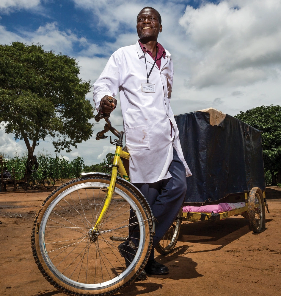 HCP wearing a medical coat pulling a cart bicycle in rural african village