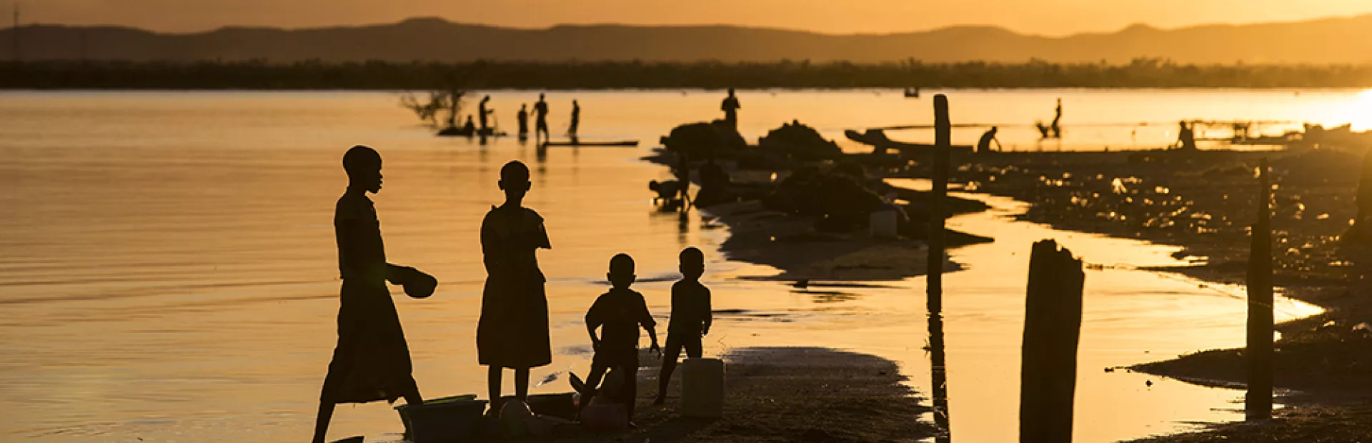 People silhouetted against the sunset on the shore of Lake Victoria, Kenya 