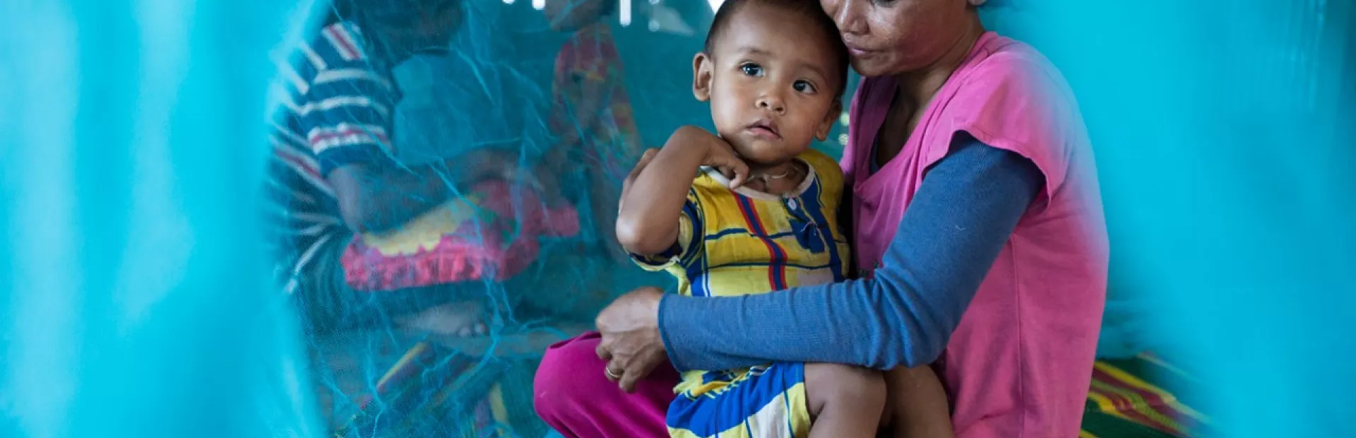 A mother and her child sit under their new insecticide-treated net in Prongyeang, Kanthout commune, Cambodia