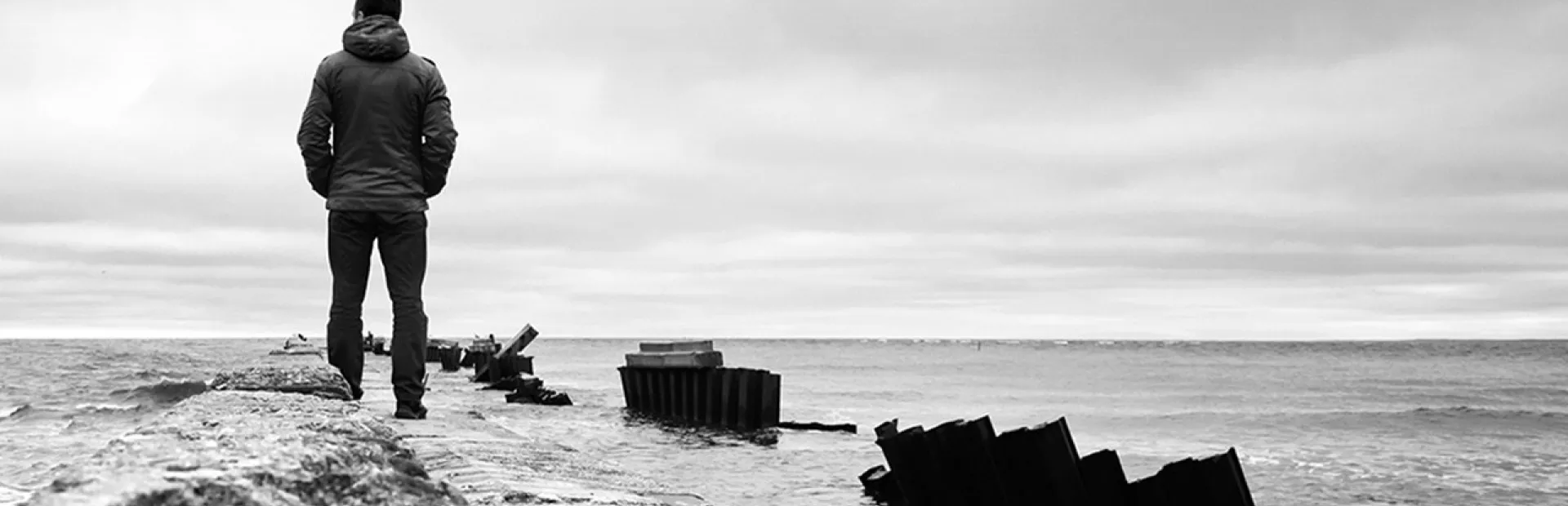 Black and white photography of a man by the shore staring at the sea