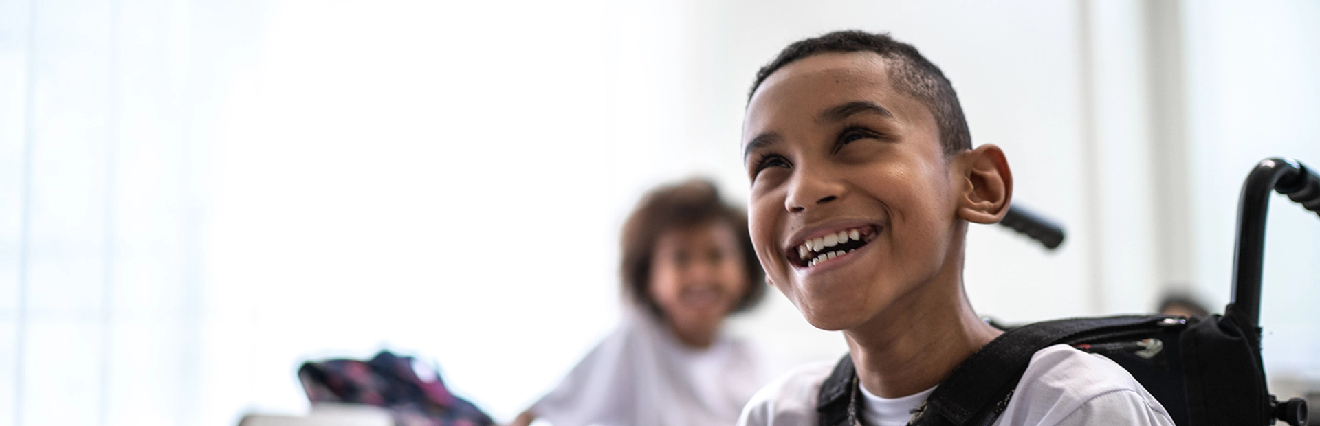Young, smiling boy in wheelchair sits next to friend in classroom