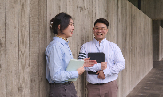 Two business people smiling and standing against a wall