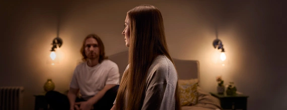 Young couple looking puzzled and sitting on their bed in a dark room