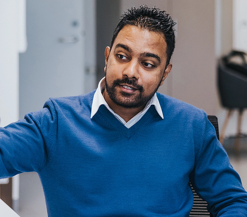 A man, seated in an office, pointing at a computer screen