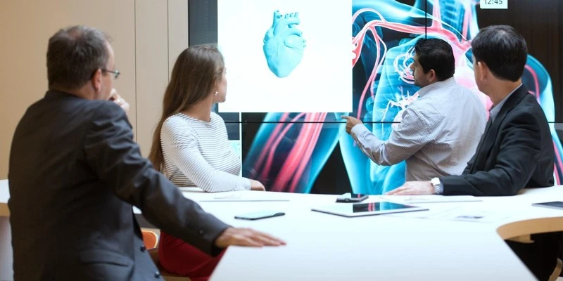 Business people examine a 3-dimensional rendering of a heart on a large screen