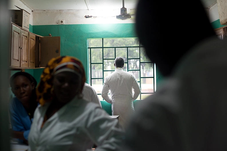 A man in a white lab coat looks out the window