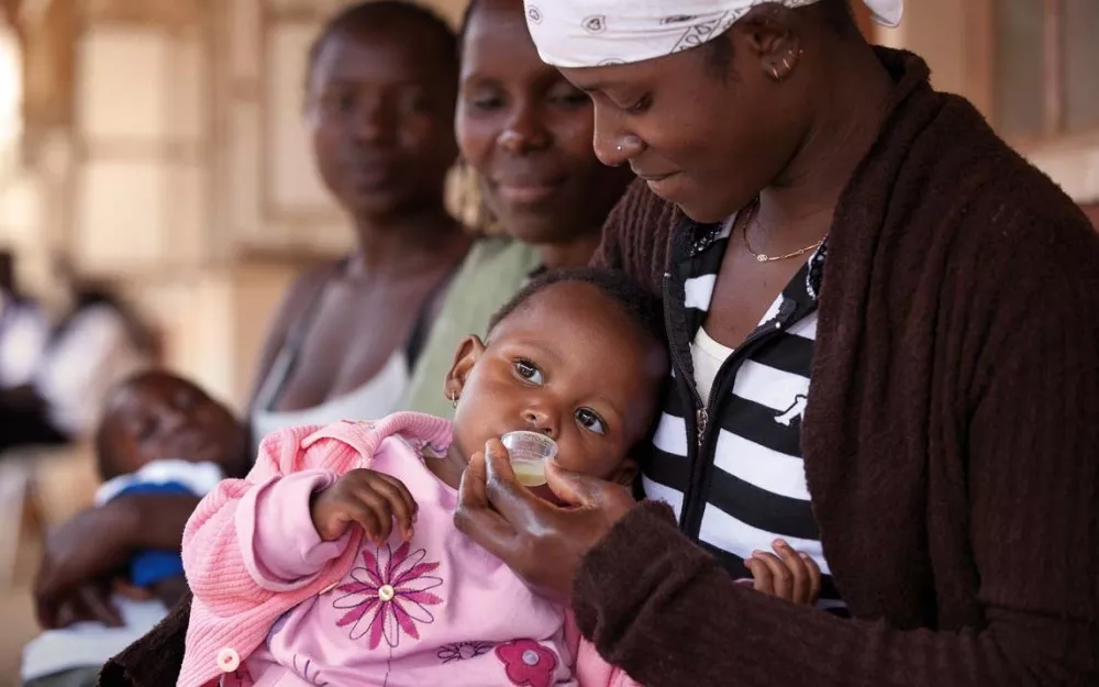 Mother gives child dispersible malaria treatment in a clinic in Kenya.