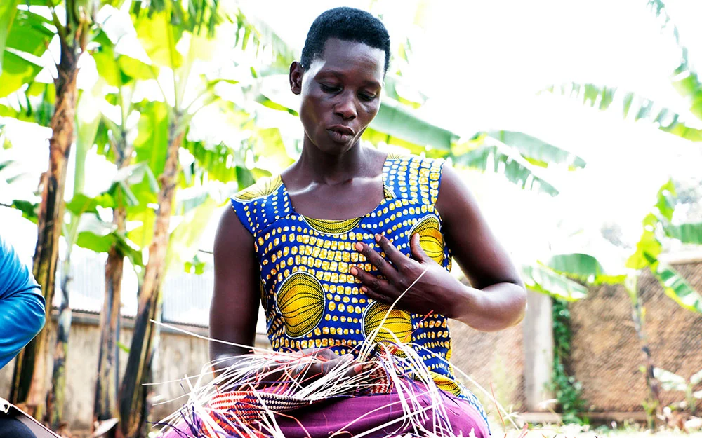 Akello sits in a garden waving a mat