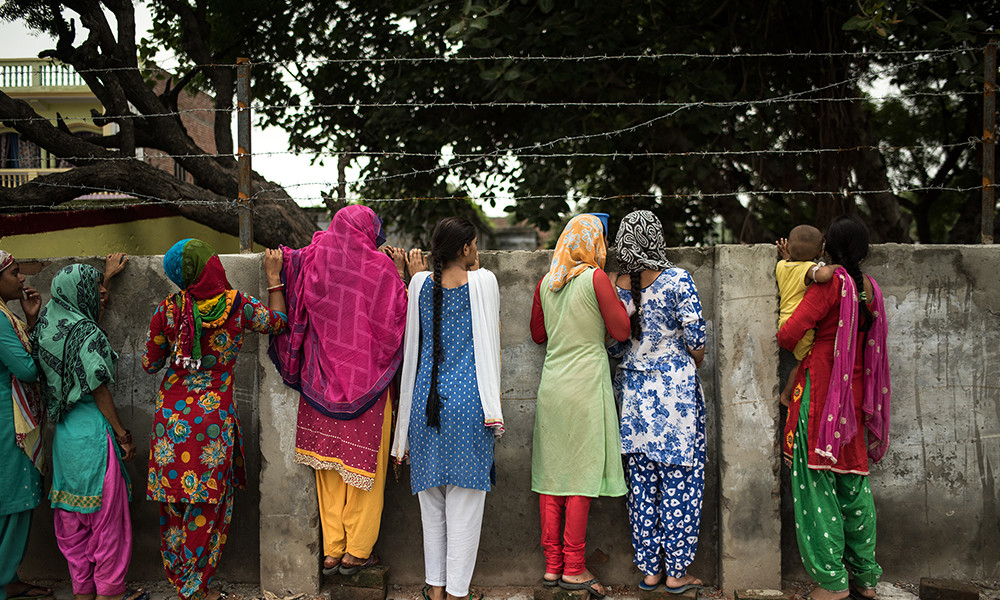 Young children peer over a wall in the Indian Village of Mulehra.