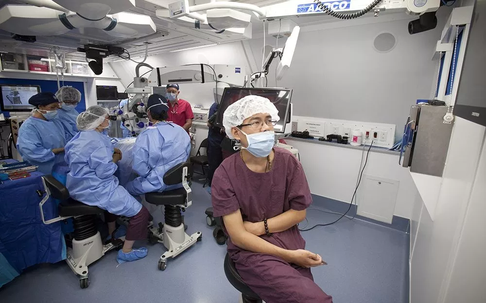 Dr. Zhang observes a surgery on a screen as trainees work in the background