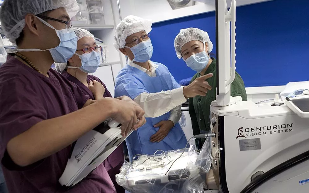 Doctors and trainees point at the screen on a medical robot that aids in eye surgeries