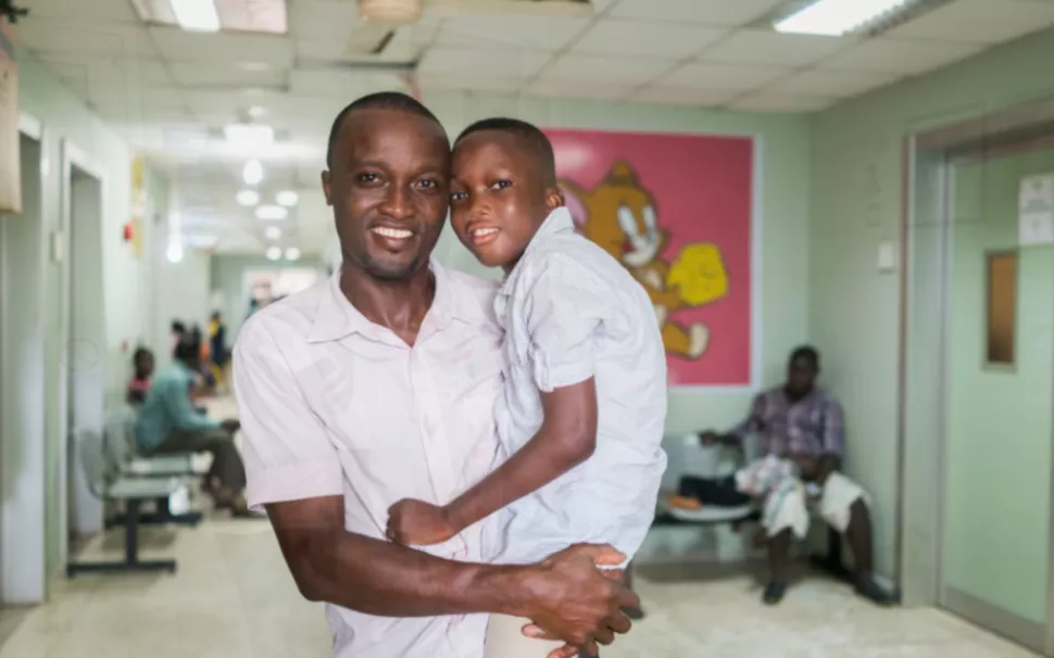 A father stands with his son in a sickle cell clinic in Ghana