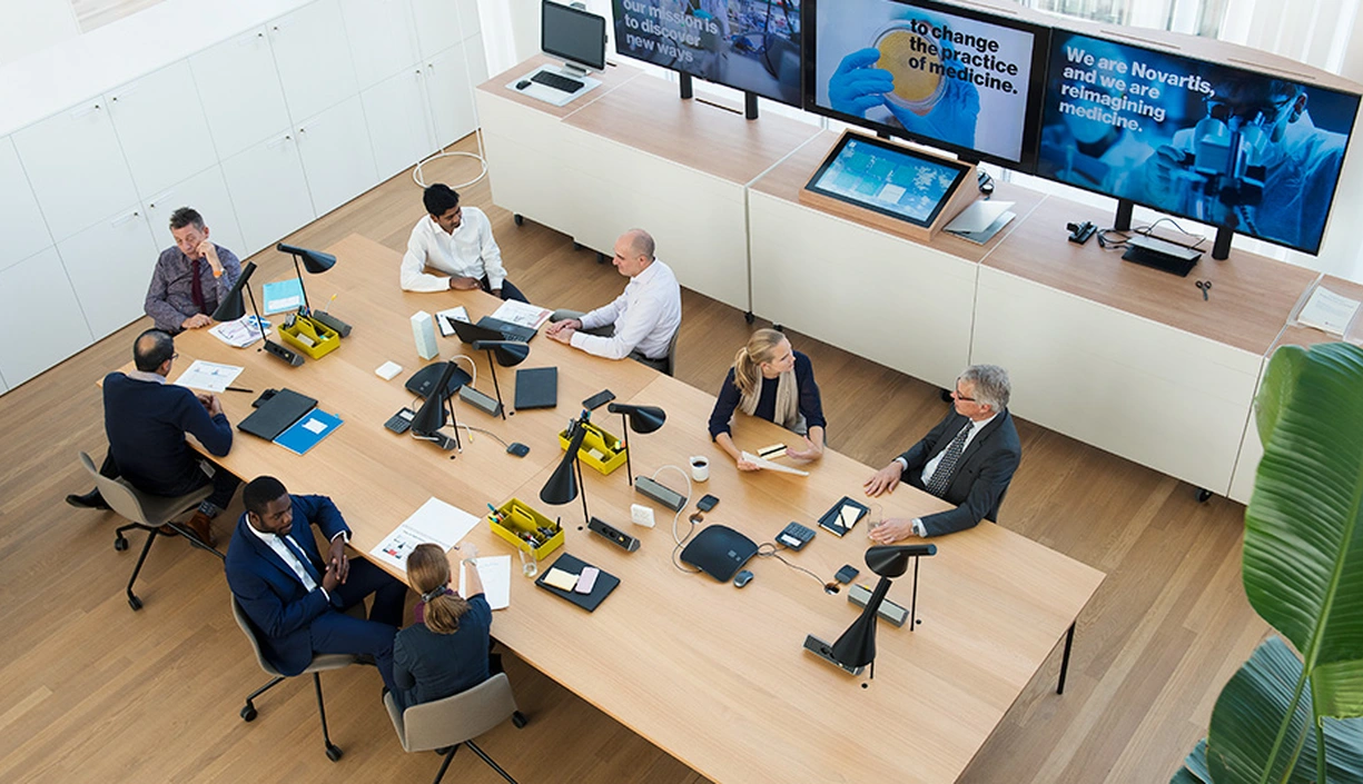 Overhead view of a meeting room with people in the foreground and screens in the background