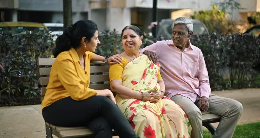 Adult daughter talking to her senior parents on a bench in a park