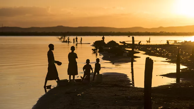 People silhouetted against the sunset on the shore of Lake Victoria, Kenya 