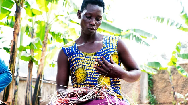 Akello sits in a garden waving a mat