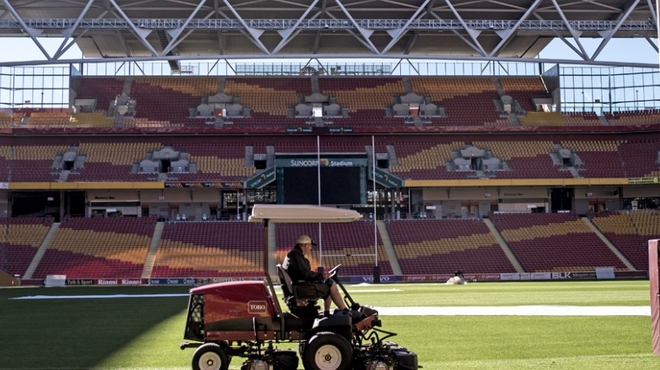 A groundskeeper drives through a stadium mowing the grass Groundskeeper Malcolm Caddies mows the grass in Brisbane, Australia