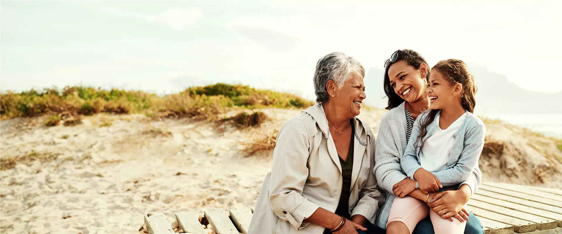 Grandmother, mother and daughter smiling and laughing on a beach