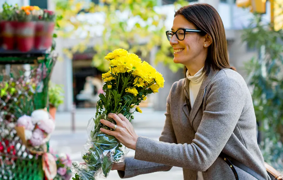 A woman holding a bunch of flowers outside a flowershop