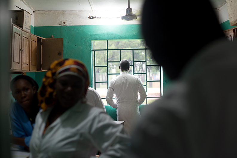 A man in a white lab coat looks out the window