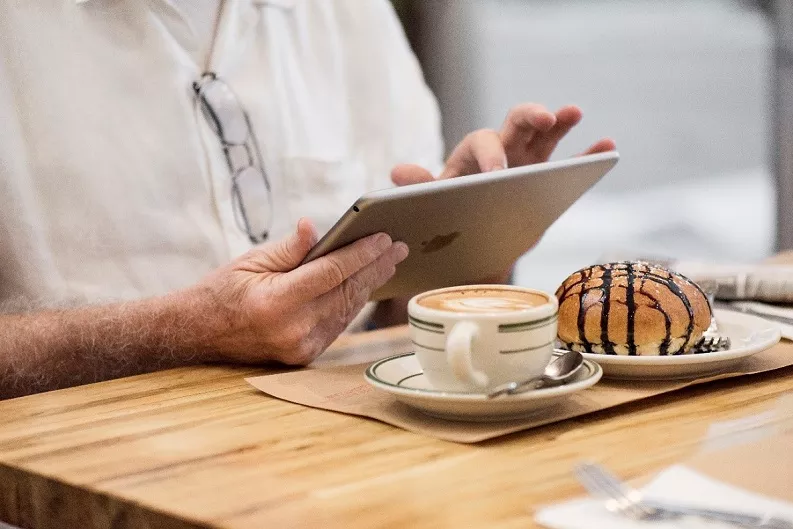 A man having coffee and looking at an Ipad