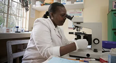 Nurse using microscope to diagnose malaria in Kenya.