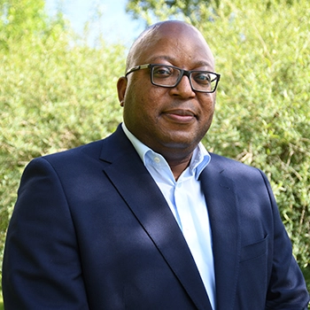 Paul Aliu, Head of the Global Governance Office in the cross-divisional Chief Medical Office at Novartis pictured in front of green bushes.