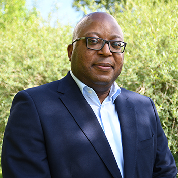 Paul Aliu, Head of the Global Governance Office in the cross-divisional Chief Medical Office at Novartis pictured in front of green bushes.