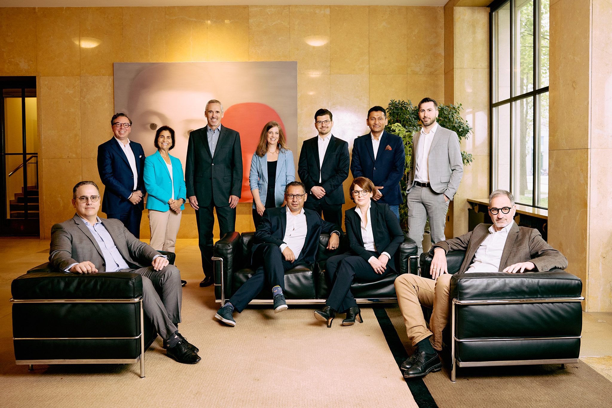 Partnering leadership team in business attire posed in a lobby with armchairs and a large artwork in the background