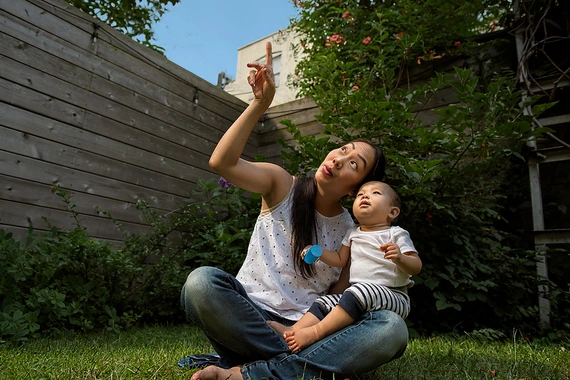 Person holding baby outdoors near gardening plants on a sunny day.