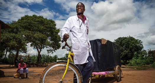 HCP wearing a medical coat pulling a cart bicycle in rural african village