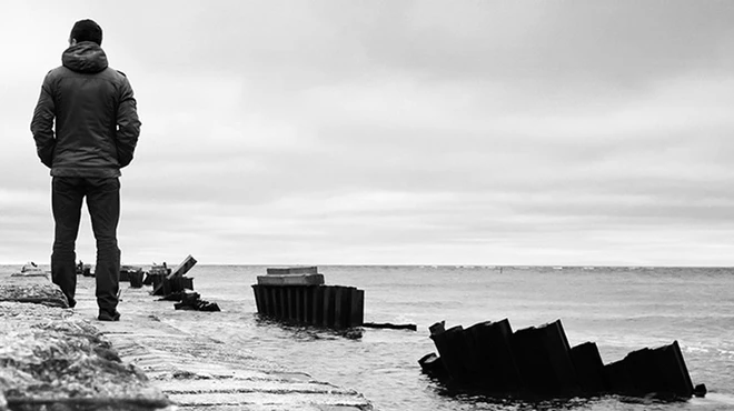 Black and white photography of a man by the shore staring at the sea