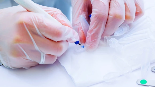 Scientist with gloves writing a number on a test tube