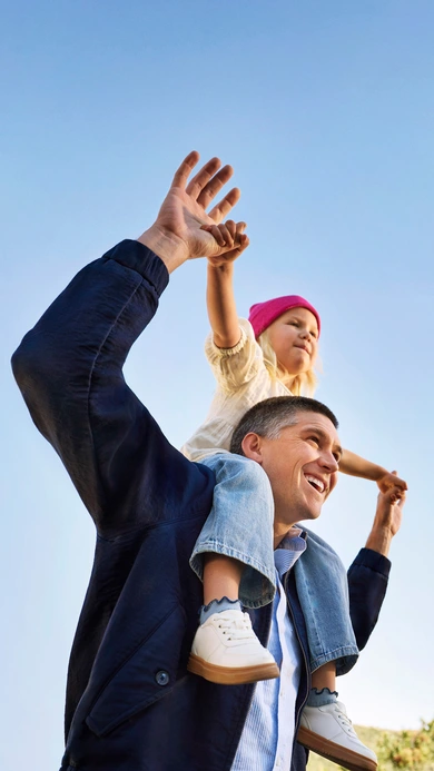 Happy father with daughter on his shoulders under a clear blue sky
