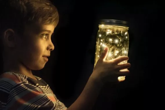 A boy looking a glow worms in a glass