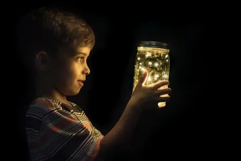 A boy looking at fireflies in a glass jar