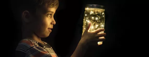 A boy looking at fireflies in a glass jar