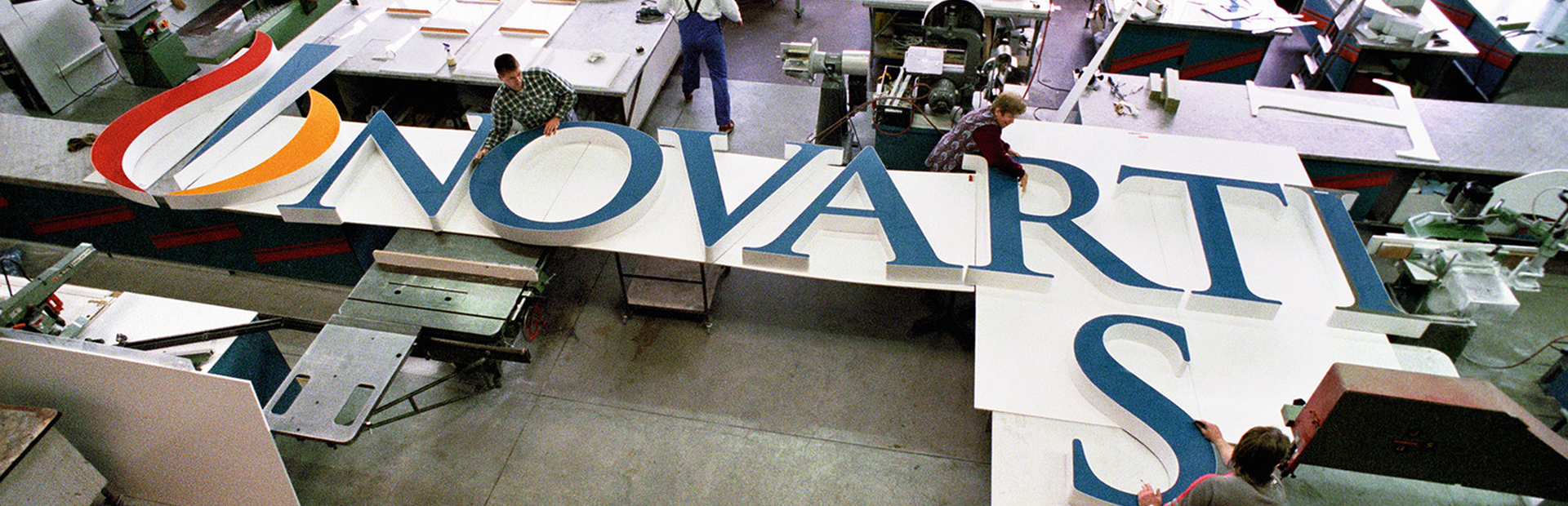 Several people working at assembling the big letters forming "Novartis" that will be installed at the top of a building on the Novartis Basel campus
