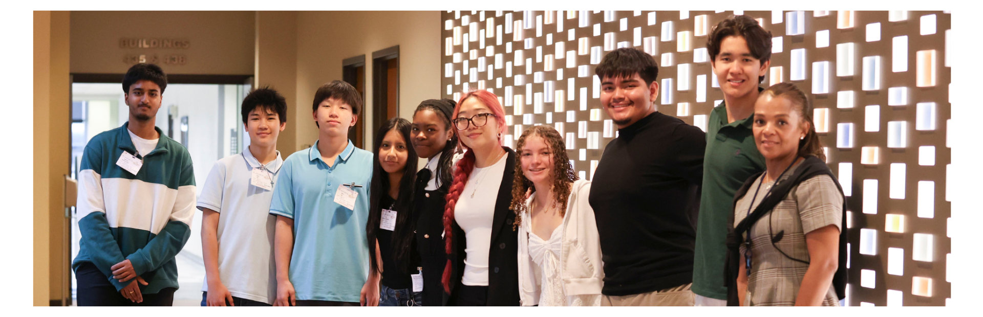 Group of students standing indoors wearing name tags in front of a patterned wall