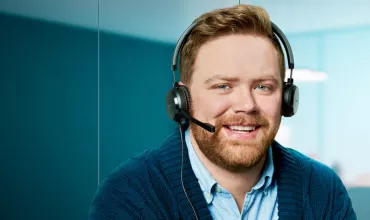 Man with headset sitting inside an office smiling 
