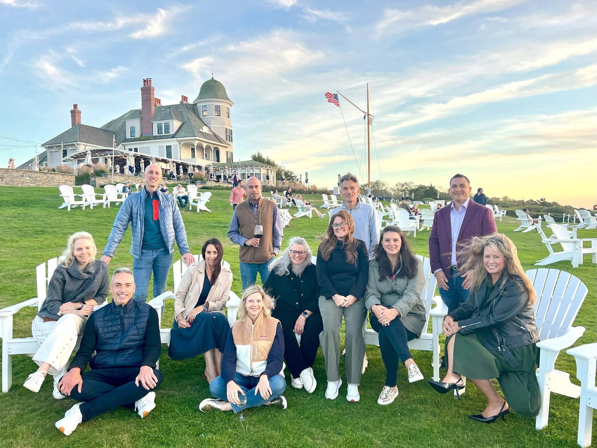 A group of people dressed in casual attire pose together on a lawn behind a large house.