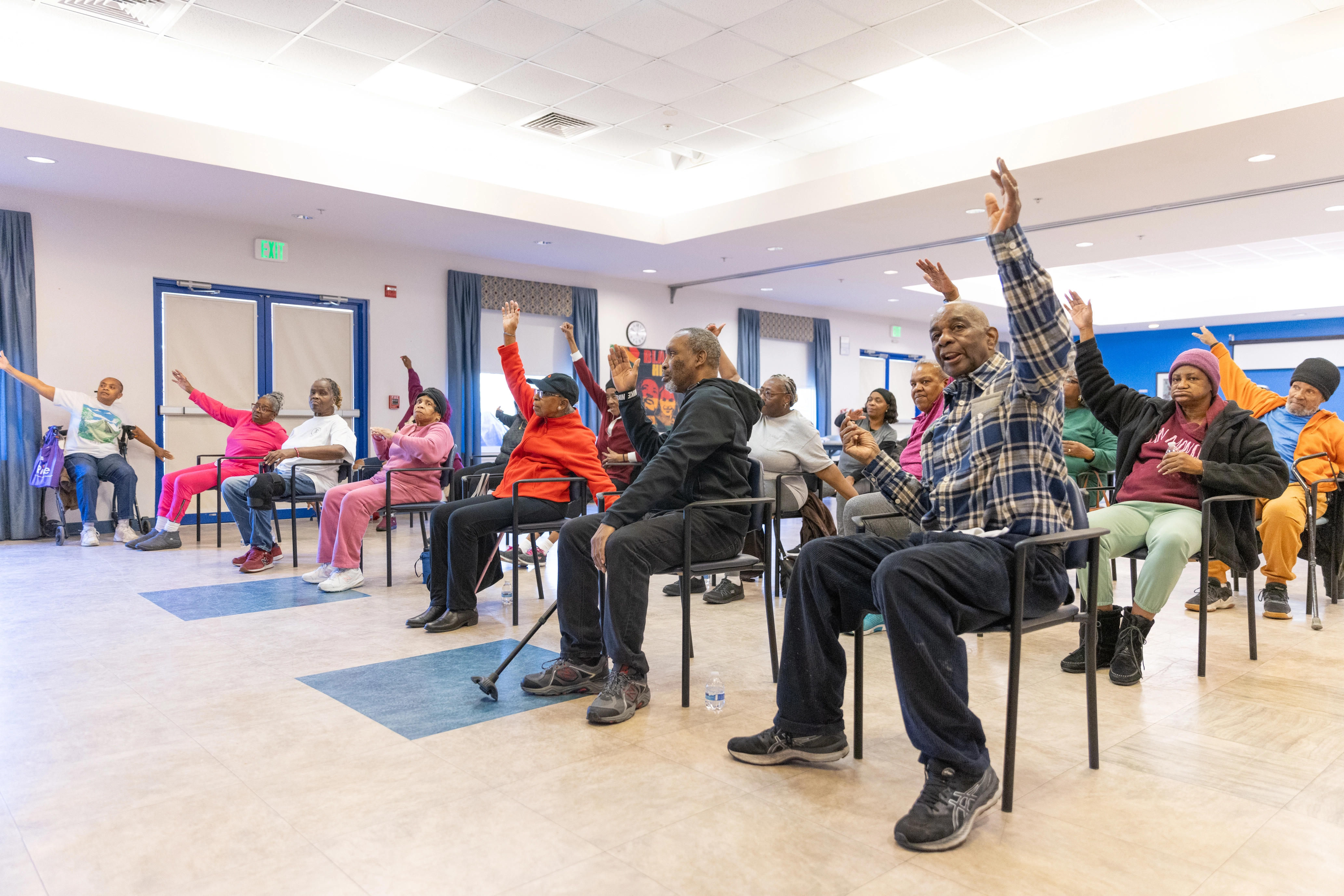 Baltimore community members participating in fitness activity as part of engAGE with Heart. The event takes place indoors and participants are raising their hands in the activity.