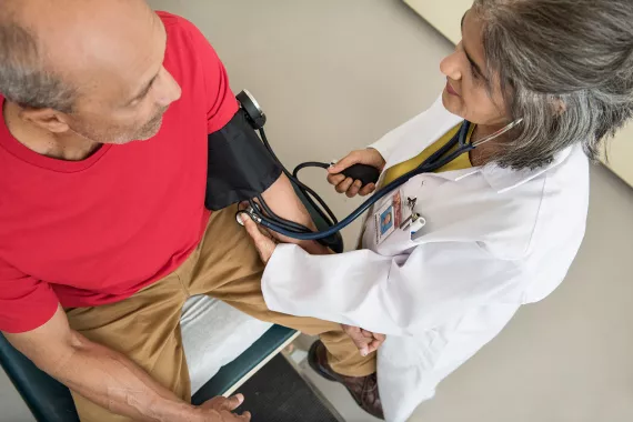 Female doctor taking the blood pressure of a male clinical trial participant.