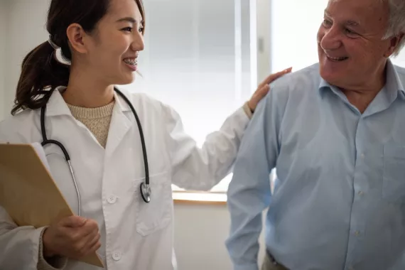 Smiling female doctor reassuring a smiling male clinical trial participant by patting him on the shoulder in a supportive manner.